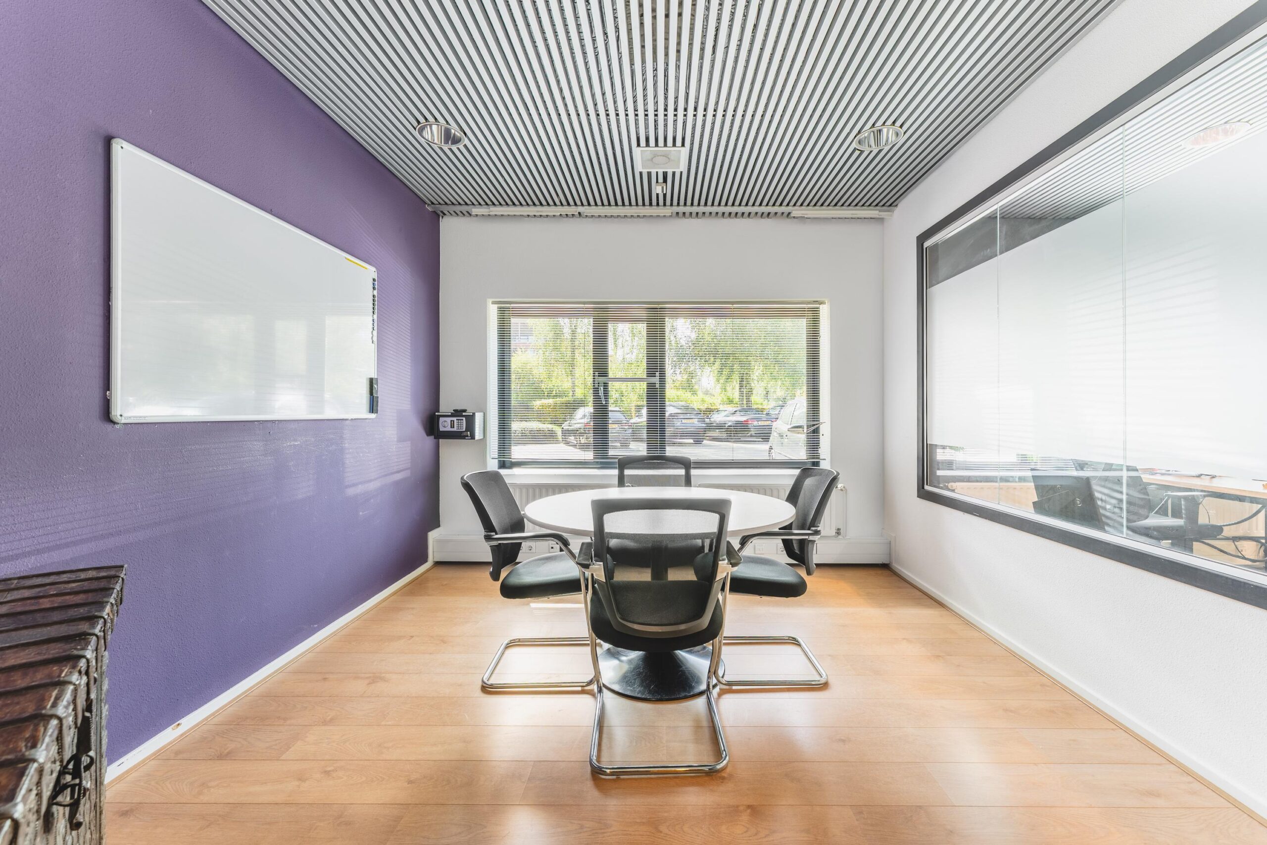 Vergaderruimte met ronde tafel, vijf stoelen, een whiteboard en groot raam aan de Prof. W.H. Keesomlaan.